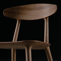 Elegant wooden chair in warm brown tones with smooth, curved lines against a black background.