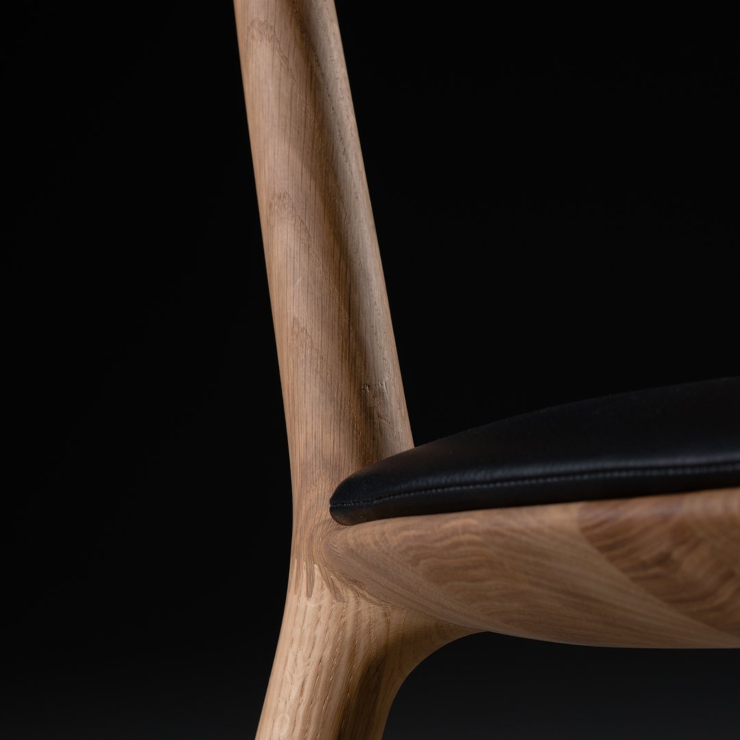 Light wood grain contrasts with a smooth black seat, featuring elegant curves and minimalistic design elements.