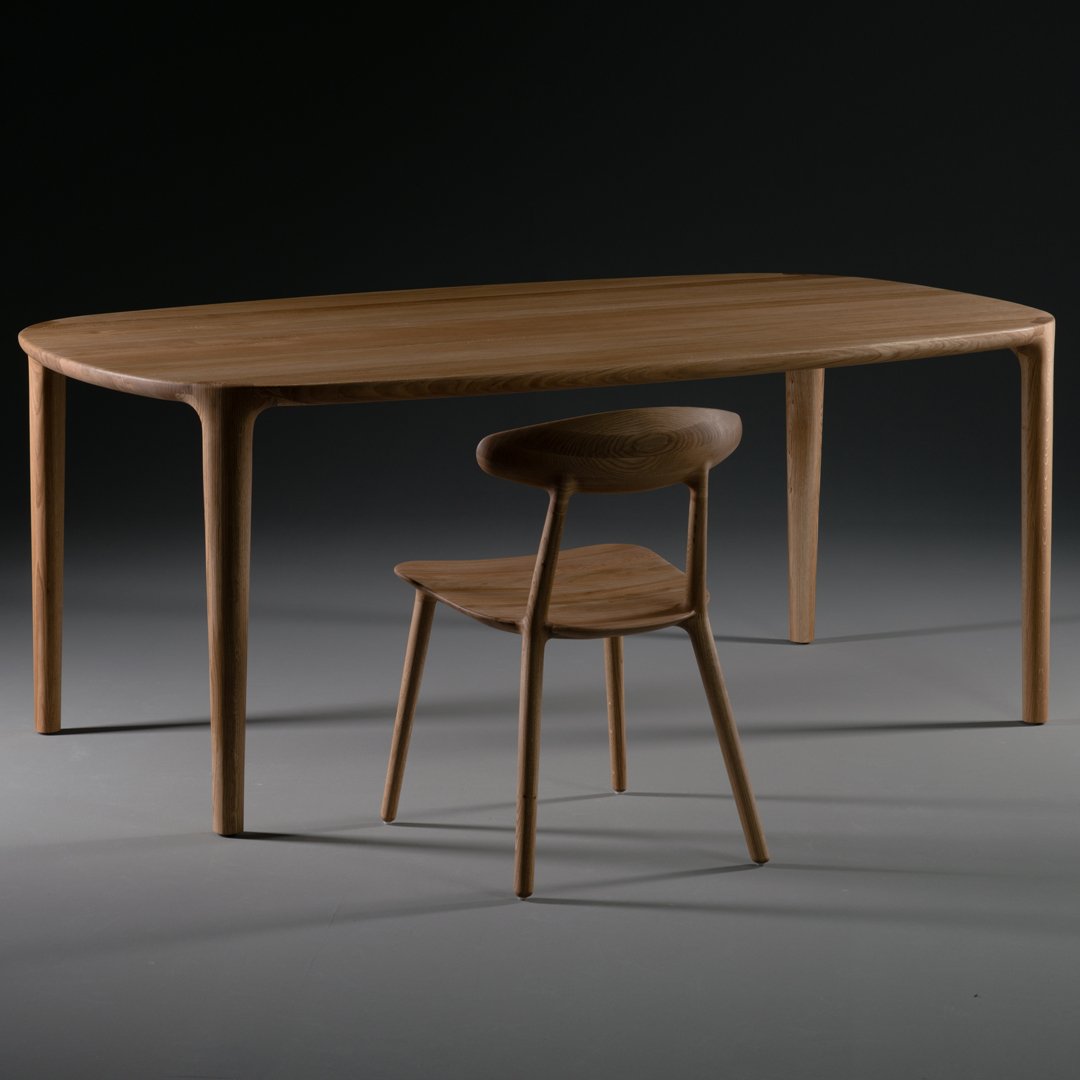 Natural wood dining table with a smooth finish and a contemporary curved design, paired with a minimalist wooden chair.