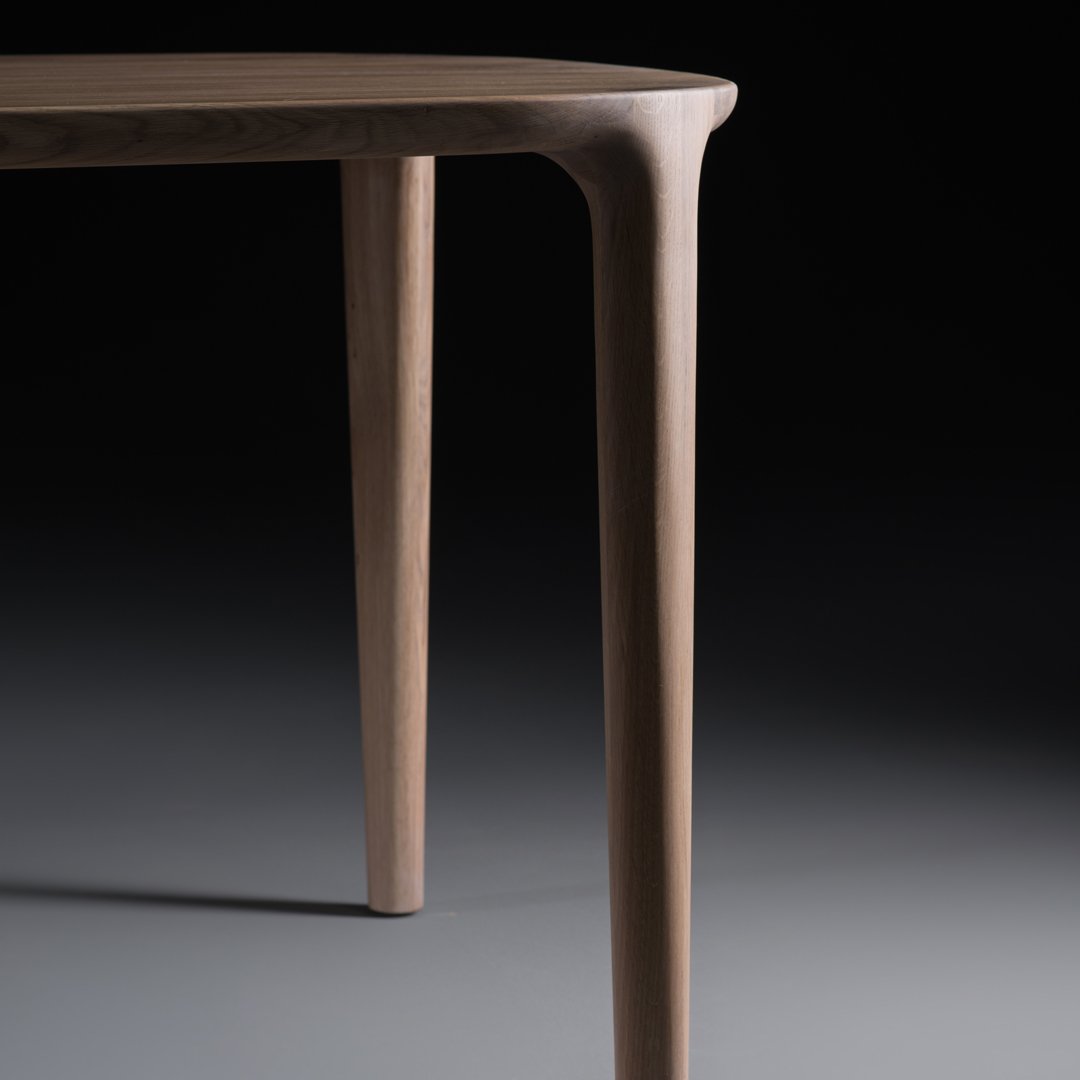 Close-up of a smooth, light brown wooden table leg against a dark backdrop, showcasing its sleek design and natural texture.