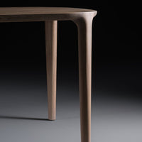 Close-up of a smooth, light brown wooden table leg against a dark backdrop, showcasing its sleek design and natural texture.