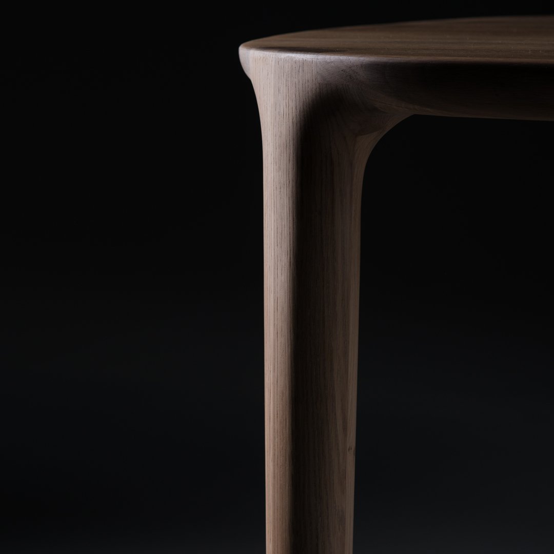 Close-up of a sleek, curved walnut table leg with a smooth, rich brown finish against a black background.