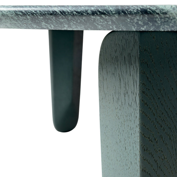 Close-up of a table featuring a textured gray surface and smooth dark green legs, highlighting natural wood grain patterns.