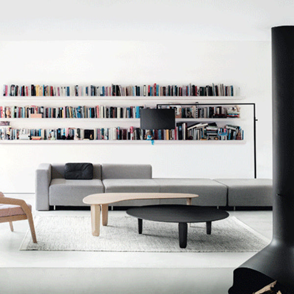 Modern living room with gray sofa, black round coffee table, and white patterned rug against a minimalist backdrop.