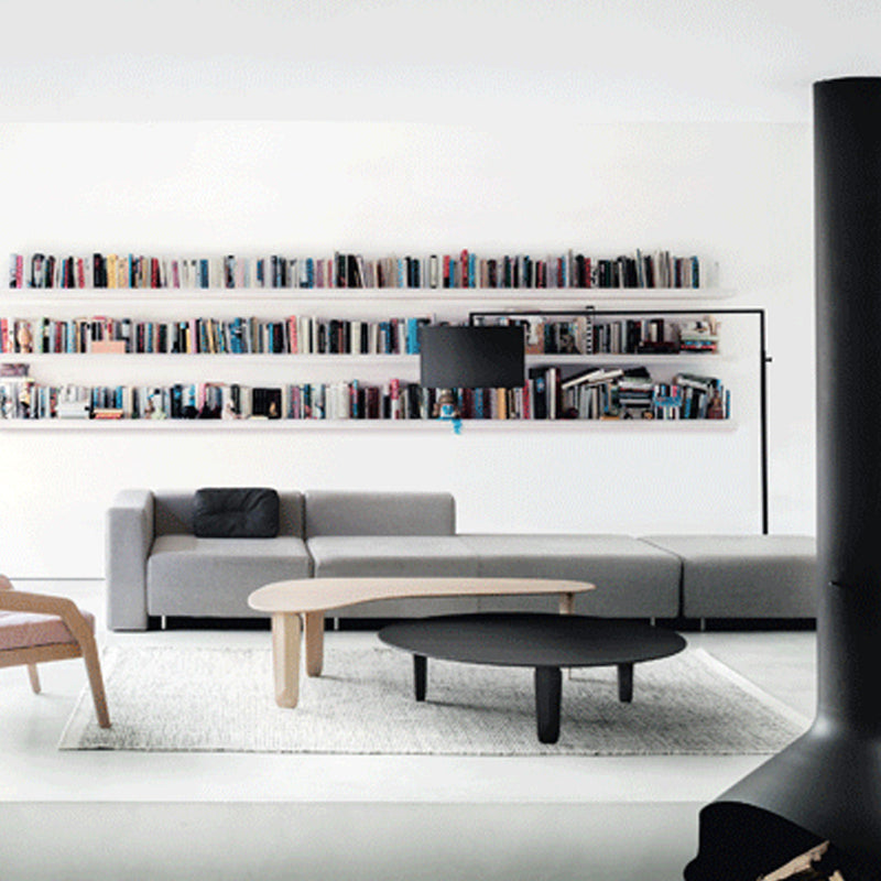 Modern living room with gray sofa, black round coffee table, and white patterned rug against a minimalist backdrop.